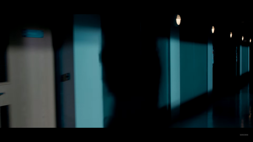 Dark hallway with teal-lit panels and a shadowy silhouette, moody and suspenseful atmosphere