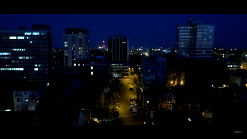 A night cityscape with illuminated high-rise buildings and streets, dark blue tones, urban mood.